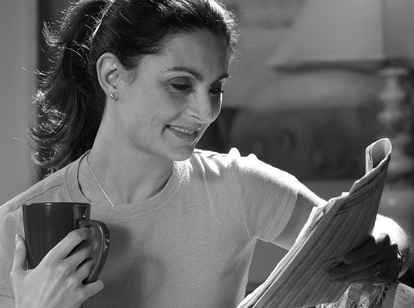 woman drinking coffee, reading newspaper